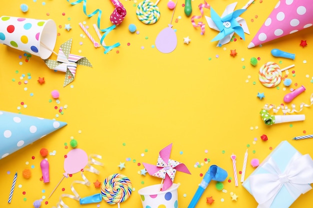 Bunte Geburtstagsmützen mit Konfetti-Lutscherbändern und Windmühlen auf gelbem Hintergrund