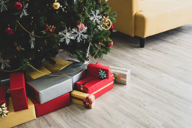 Bunte Geschenkboxen unter verziertem Weihnachtsbaum auf Bretterboden.