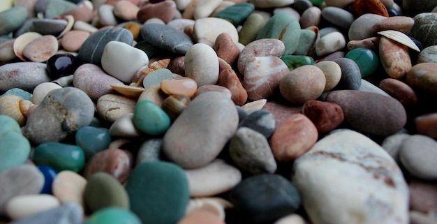 Bunte, glatte Quarzsteine auf runden Kieselsteinen, gemischt mit kleinen Muscheln, Nahaufnahme