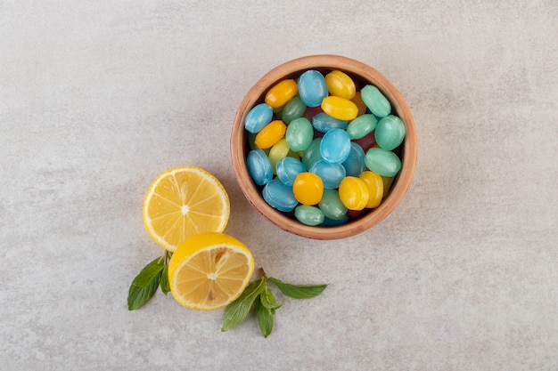 Bunte Hartbonbons in Schüssel mit geschnittener Zitrone auf Steintisch gelegt.