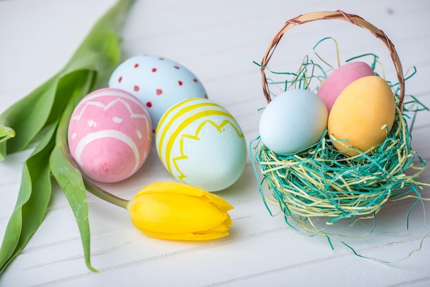 Bunte helle Ostereier mit gelben Tulip handbemalt auf weißem Holzhintergrund Festliche Frühlingskarte