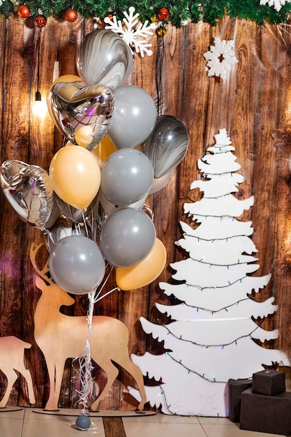 Bunte Luftballons ein weißer Weihnachtsbaum mit Girlanden Schneeflocken Hirsch auf einem hölzernen Hintergrund