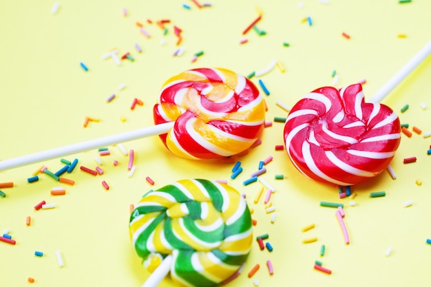 Foto bunte lutscher und konfetti auf gelbem hintergrund. süßigkeiten für die party. zucker