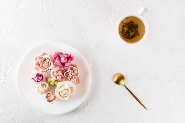 Bunte Marshmallow-Rosen auf einem Teller mit einer Tasse grünem Tee