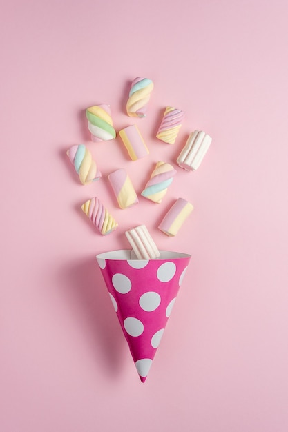 Bunte Marshmallows mit Partyhut auf rosa.