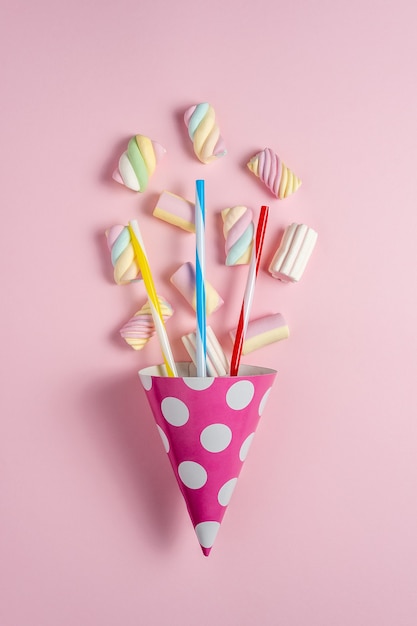 Bunte Marshmallows mit Partyhut auf rosa.