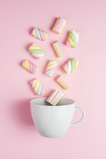Bunte Marshmallows mit weißer Tasse auf rosa Oberfläche