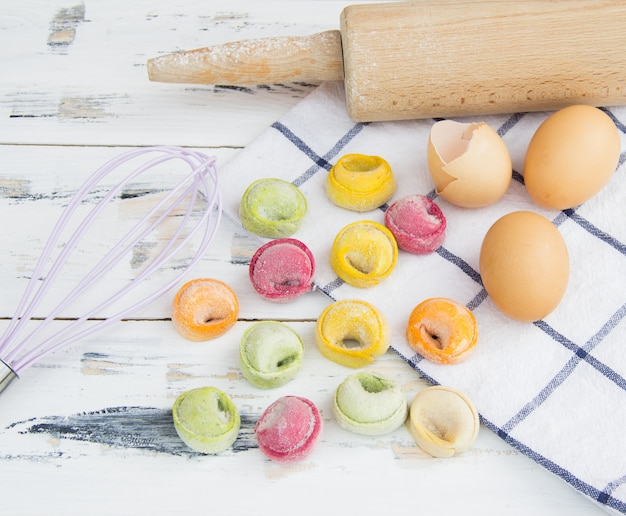 Bunte Mehlklöße mit Küchengeschirr, Eiern und Serviette auf weißem Holztisch.