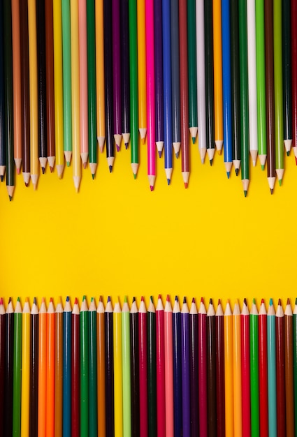 Bunte mehrfarbige Stifte auf gelbem Hintergrund. Draufsicht, Kopierraum