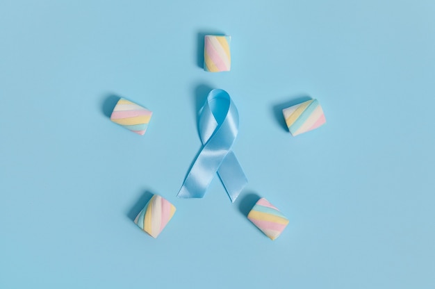 Bunte, mehrfarbige, zuckerhaltige Marshmallows, die in einer fünfzackigen Sternform mit einem blauen Bewusstseinsband auf einem pastellfarbenen Hintergrund mit Kopierraum ausgelegt sind. Konzept zum Weltdiabetestag 14. November