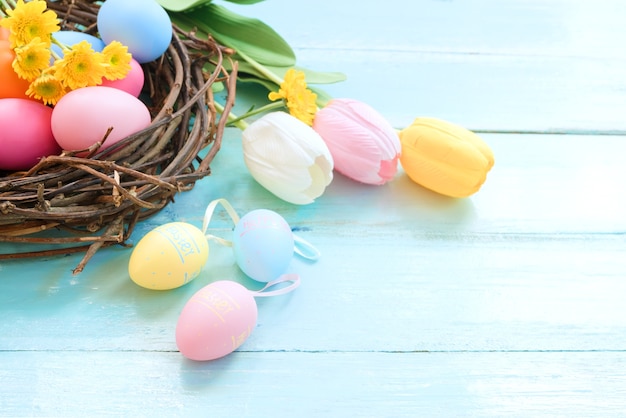 Bunte Ostereier im Nest mit Blumen auf blauem hölzernem Hintergrund