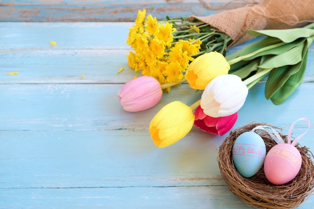 Bunte Ostereier im Nest mit Blumen auf blauem hölzernem Hintergrund.