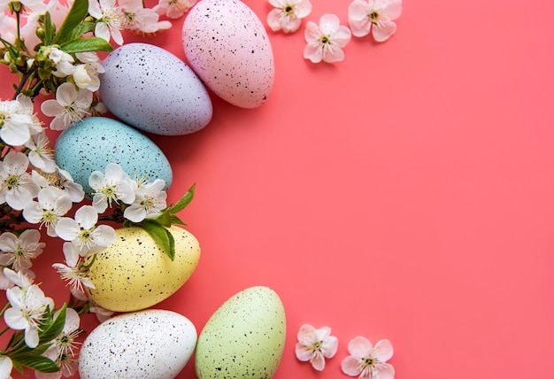 Bunte Ostereier mit Frühlingsblütenblüten über rosa Hintergrund.