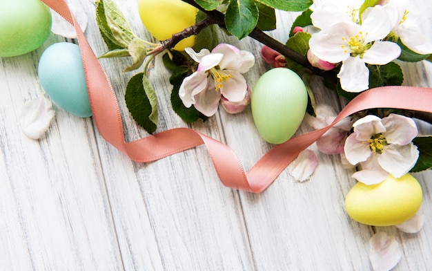 Bunte Ostereier mit Frühlingsblütenblumen über hölzernem Hintergrund.