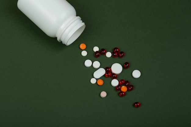 Bunte Pillen des Medizinkonzeptes und weiße medizinische Flasche auf Grünbuchhintergrund