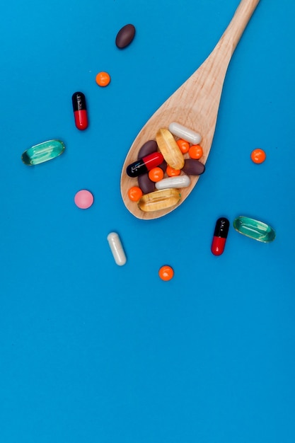 bunte Pillen in einem Holzlöffel auf blauem Hintergrund