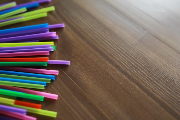 Bunte Plastiktrinkhalme schließen sich als hintergrundfarbene Röhrchen für Saft und Cocktails auf schwarzem Holztisch