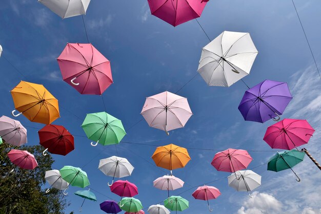 Bunte Regenschirme hängen vom Draht mit Wolke des blauen Himmels im Hintergrund