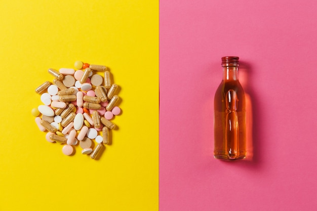 Bunte runde Tabletten der Medikation angeordnet abstrakt, Flaschenalkohol auf gelbem rosa Hintergrund