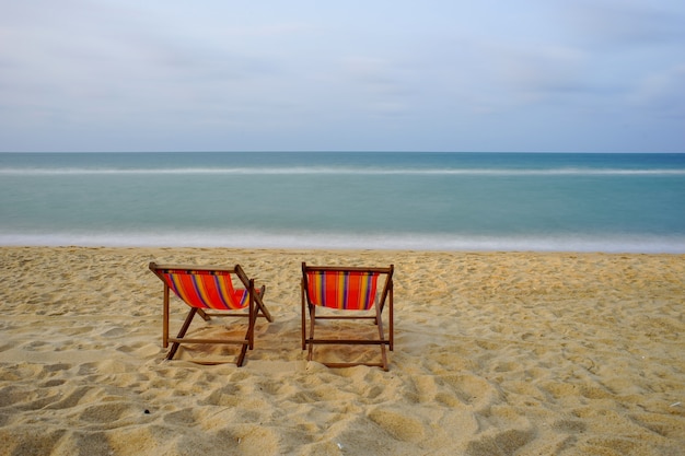 Bunte Stühle am Strand mit Sommersonne, klarem Meerwasser und blauem Himmel.