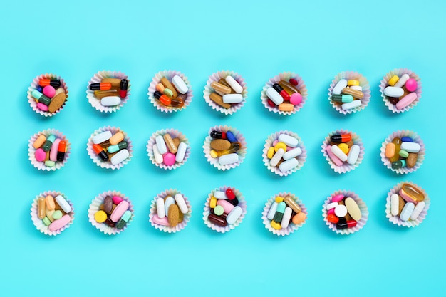 Bunte Tabletten mit Kapseln und Pillen in Cupcake-Verpackungen auf blauem Hintergrund.