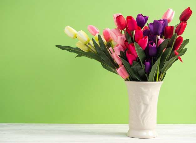 Bunte Tulpen im Vase auf weißem Tabellenwand-Grünhintergrund