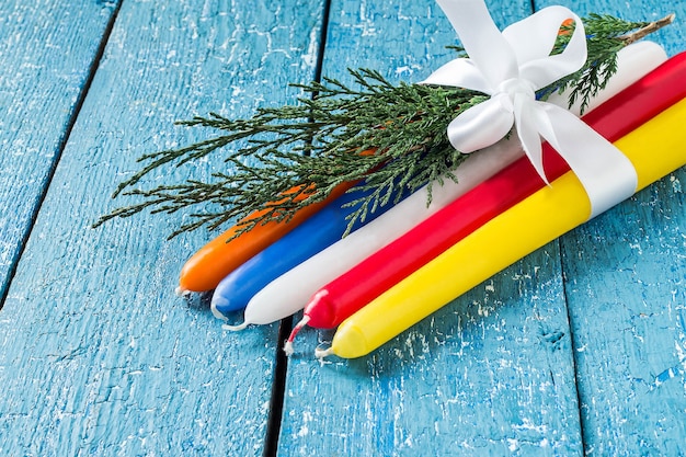 Bunte Weihnachtskerzen mit Nadelzweig und weißer Schleife auf blauem Holztisch