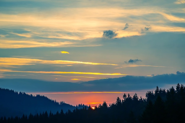 Bunte Wolken am Himmel bei Sonnenuntergang vor der Kulisse eines bergigen Waldgebietes