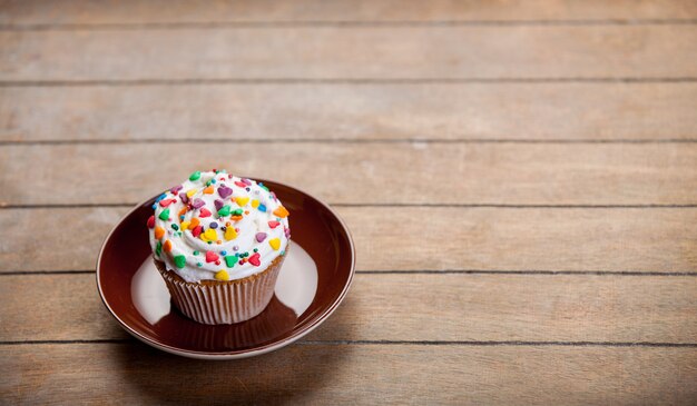 Bunter Cupcake auf einem Teller und Holztisch.