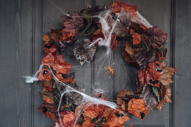 Bunter Kranz für Halloween, der an der Holzhaustür aus alten orangefarbenen Ahornblättern hängtSpinnennetzDekoration der VerandaZuhause im FreienStraßendekorationUnterhaltung für KinderHorroratmosphäre