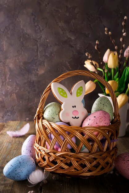 Bunter Osterei- und Plätzchenhäschen im Korb und in den Tulpen blüht auf Holztisch.