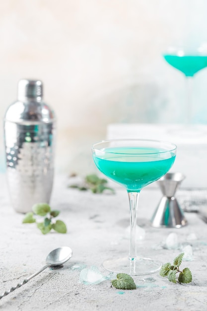 Bunter Sommercocktail Blue Hawaii oder eisgekühltes blaues Lagunen-Alkoholgetränk mit Minze auf hellem Steinhintergrund