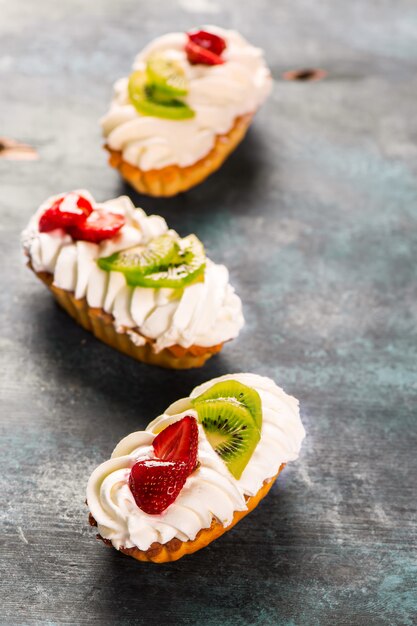 Buntes Gebäck backt mit Schlagsahne, Früchten und Beeren auf blauem hölzernem Hintergrund des Schmutzes zusammen