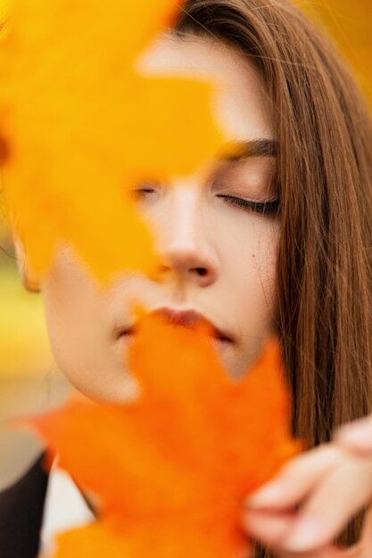 Buntes Herbstporträt eines schönen jungen sinnlichen Mädchens mit geschlossenen Augen in einem Herbstpark mit hellen gelborangen Blättern