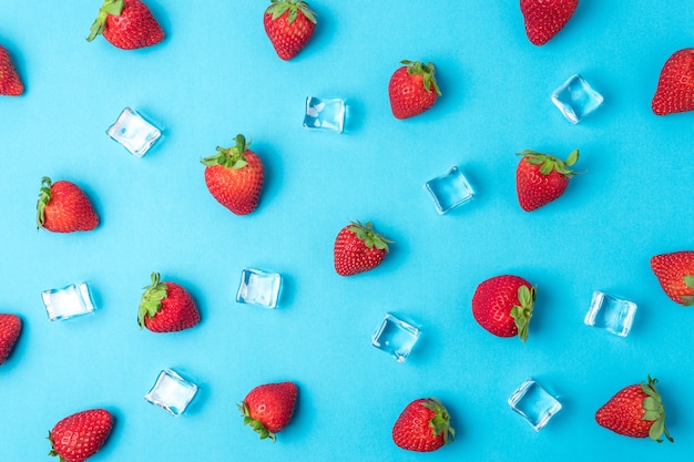 Buntes Muster aus Erdbeeren mit Eiswürfeln auf blauer Oberfläche.