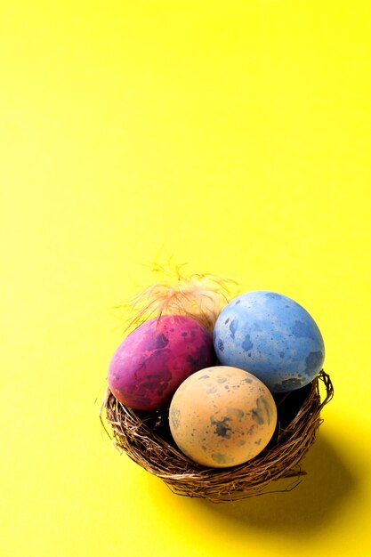 Buntes Osterei im Nest auf gelbem Hintergrund mit Kopienraum. Ostern Hintergrund Minimalismus