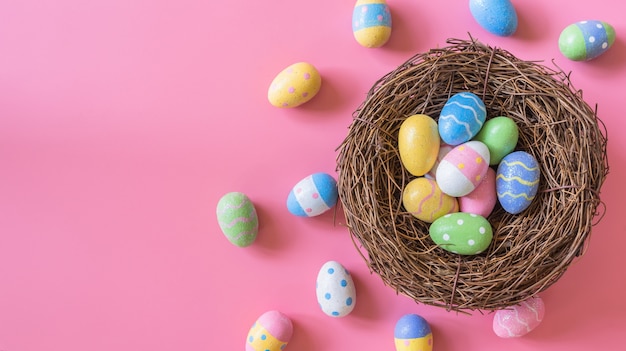 Buntes Osterei und Nest auf rosa Pastellfarbhintergrund mit Raum.