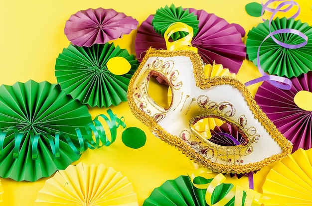 Buntes Papierkonfetti, Karnevalsmaske und farbiger Serpentin auf gelbem Grund
