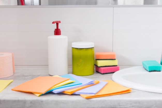 Buntes Set von Haushaltsputztüchern, die neben dem Handwaschbecken in einem Badezimmer mit Schwämmen und Seife dahinter ausgebreitet sind