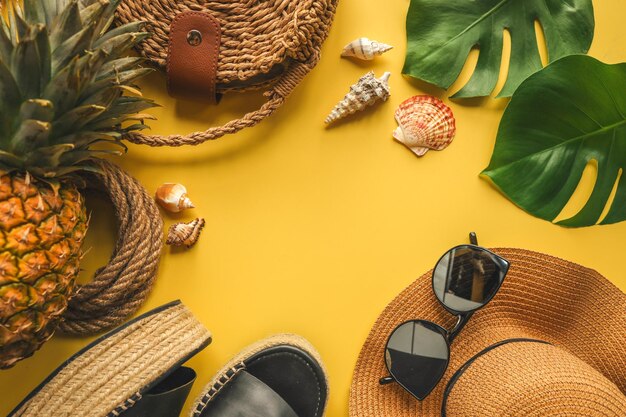 Buntes Sommermode-Outfit flach lag Strohhut Korbschuhe Ananas über gelbem Hintergrund Draufsicht breite Komposition Sommermode-Urlaubskonzept