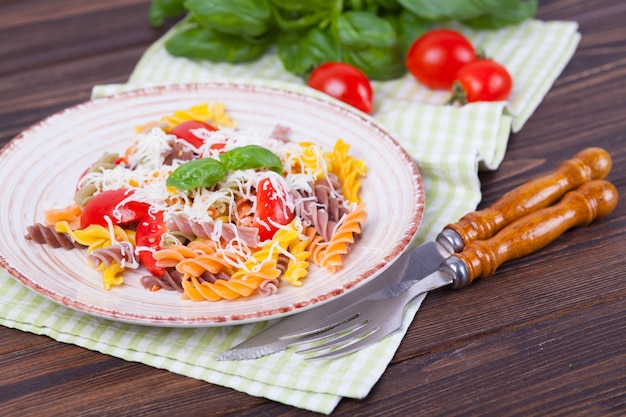 Buntes Teigwaren fusilli mit Tomate, Basilikum und Käse auf einem dunklen Holztisch