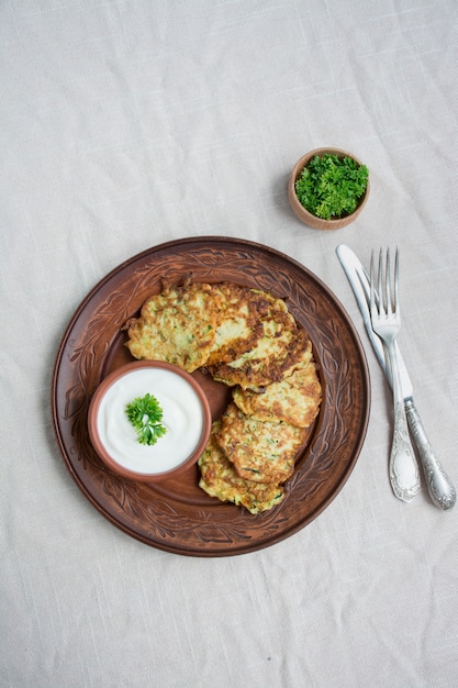 Buñuelos de calabacín. Crepes de calabacín vegetarianos servidos con hierbas frescas y crema agria. Fondo claro.