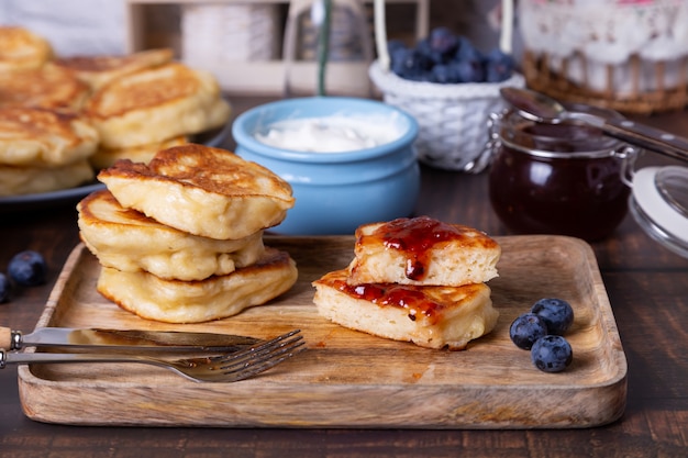 Buñuelos con crema agria, mermelada y arándanos. El plato tradicional ruso. De cerca.