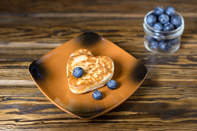 Buñuelos de panqueques en forma de corazón con arándanos en un plato de estilo rústico Primer enfoque selectivo