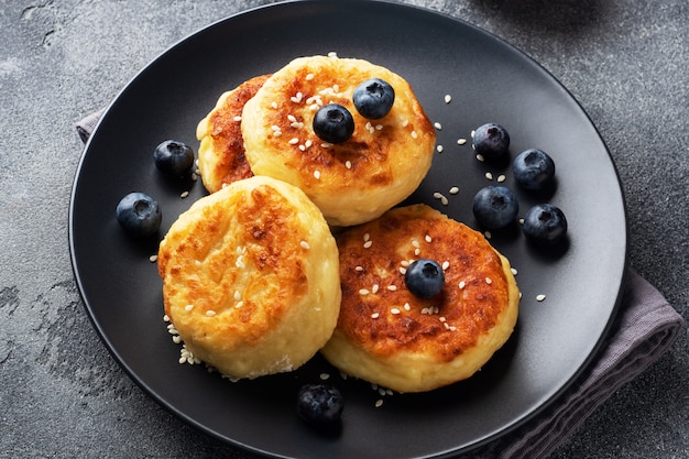 Buñuelos de requesón con arándanos. Tartas de queso cuajada de queso, panqueques en una mesa de hormigón oscuro. Copia espacio