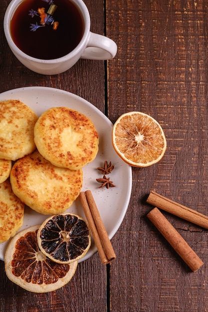 Buñuelos de requesón con té aromático negro caliente, humor de desayuno de Navidad con anís, canela y cítricos secos sobre fondo de madera, vista superior