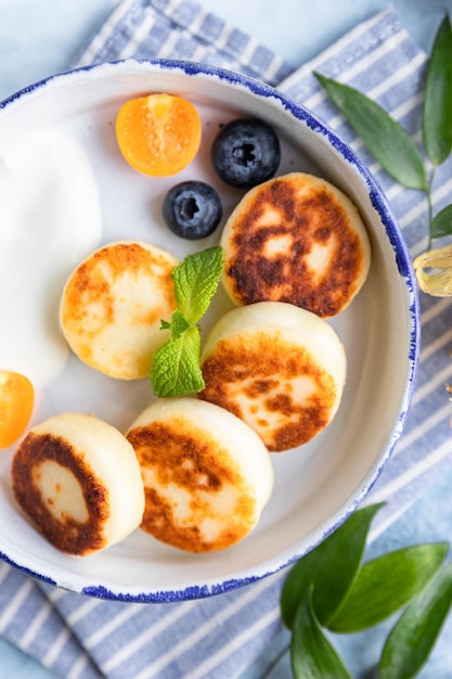 Foto buñuelos de tortitas de queso o syrniki con physalis de arándanos y yogur desayuno saludable y sabroso