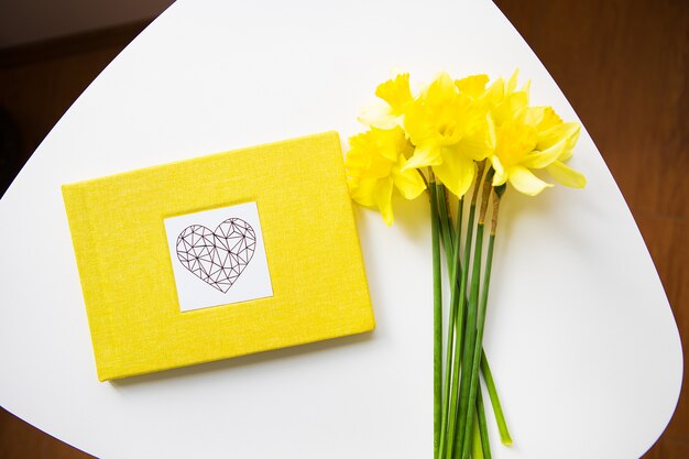 Buquê amarelo de narcisos e livro amarelo na mesa branca