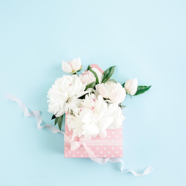 Buquê branco de peônias em um envelope para flores em fundo azul conceito floral mínimo saudação