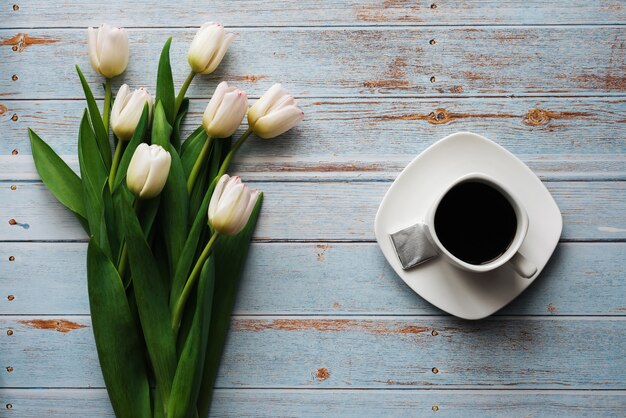 Buquê branco de tulipas em um fundo azul de madeira com uma xícara de café